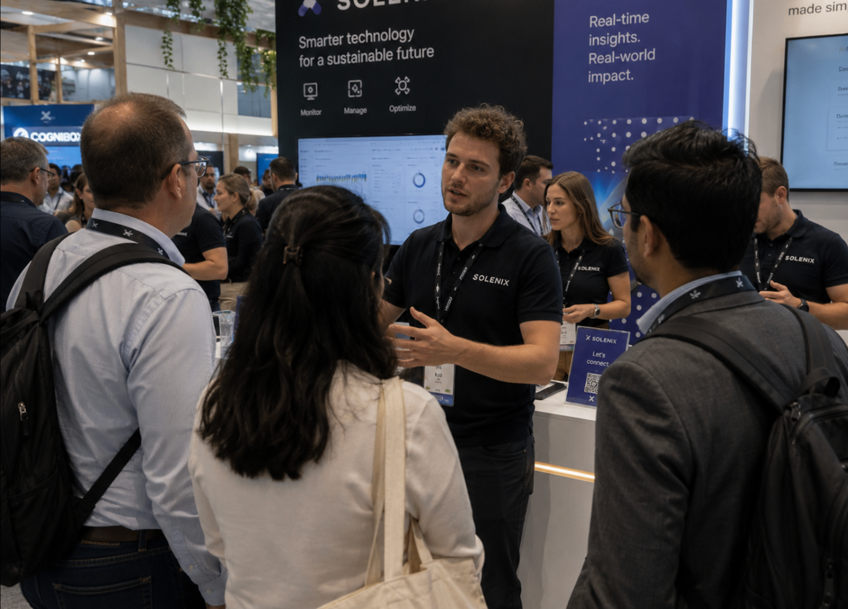 Trade show booth staff in branded black polos pitching a tech product to attendees at an industry expo