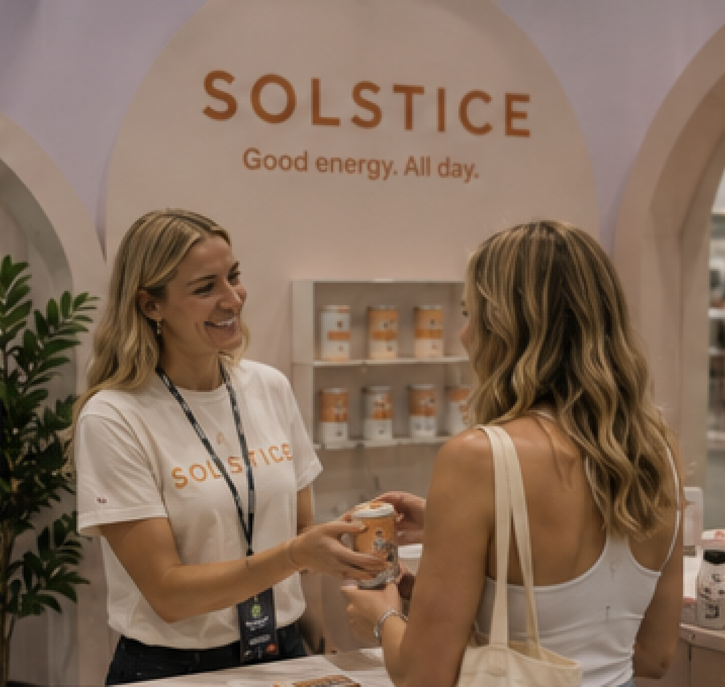Brand ambassador in a white branded T-shirt serving a guest at a pastel exhibition stand
